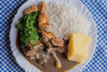 a white plate topped with rice meat and vegetables on a checkered table cloth