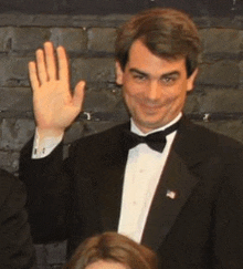 a man in a tuxedo is waving his hand