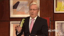 a man in a suit and tie is holding a cucumber in front of a wall that says meet the press on it