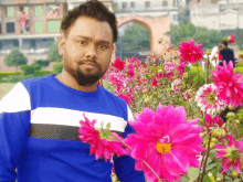 a man in a blue and white shirt stands in front of a bunch of pink flowers