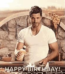 a man in a white shirt is standing in front of a stove cooking food and says `` happy birthday '' .