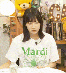 a woman wearing a mardi t-shirt is sitting at a table with a bottle of water in front of her .