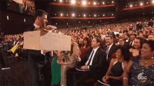 a man in a suit is holding a cardboard box in front of a crowd of people at an abc event