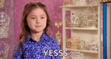 a little girl in a blue shirt is standing in front of a shelf with a shelf full of trophies .