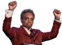 a woman in a red jacket stands at a podium with her arms in the air