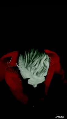 a man with white hair and a red jacket is sitting in a dark room with his head down .