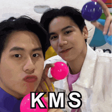 two young men holding pink and blue balls with kms written on the bottom