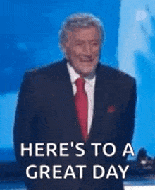 a man in a suit and tie is saying `` here 's to a great day '' while standing on a stage .