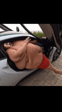 a very fat man is sitting in the back of a car with the trunk open .