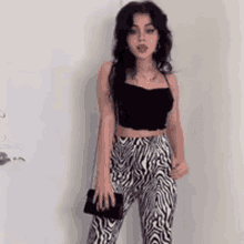 a woman in a black crop top and zebra print pants is standing in front of a white wall .