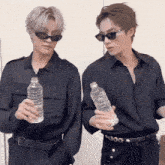 two men wearing black shirts and sunglasses holding bottles of water