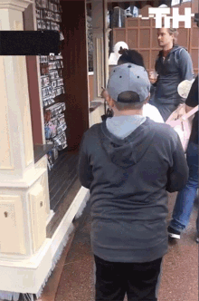 a man wearing a baseball cap stands in front of a store with a sign that says th on it