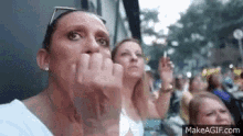 a group of women are sitting in a crowd and one of them is covering her face with her hand .