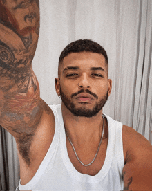 a man with a tattoo on his arm is wearing a white tank top and a silver chain