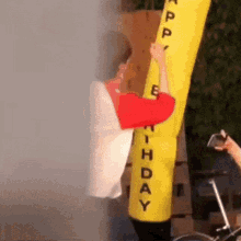 a man in a red and white shirt is climbing up a yellow inflatable balloon that says happy birthday .