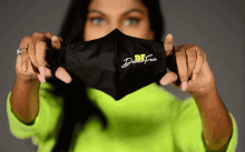 a woman in a neon green sweater is holding a black face mask with dare fun written on it