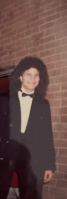 a man in a tuxedo stands in front of a brick building