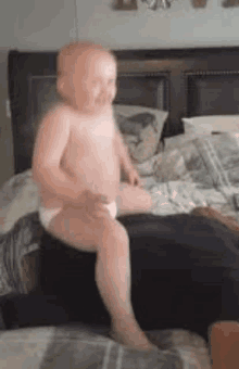 a baby in a diaper is sitting on a bed with a person .