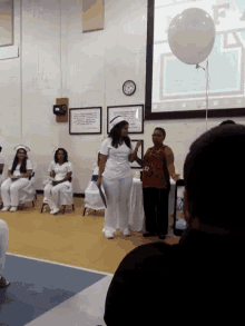 a woman in a nurse 's cap and gown stands in front of a large white balloon that says " f "