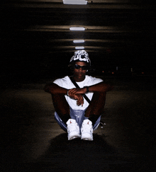 a man wearing sunglasses and a hat with the letter u on it sits on the ground