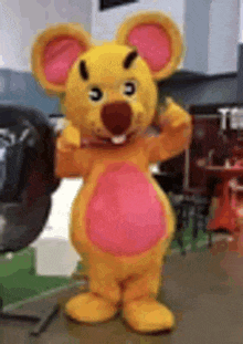 a yellow mascot costume of a mouse is standing on a table .