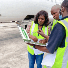 a woman in a yellow vest is looking at a laptop with a green circle on the screen that says gmd