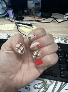 a woman 's hand with christmas nails and a bottle of second choice on the desk