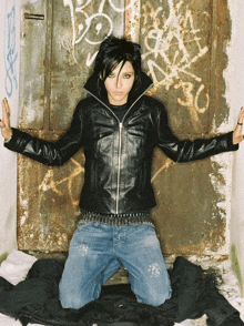 a woman wearing a black leather jacket is kneeling down in front of a door with graffiti on it