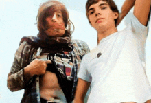 a man in a white t-shirt is standing next to a woman in a plaid shirt who is taking off her shirt