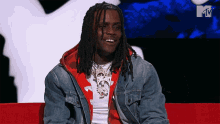 a man with dreadlocks is sitting on a red couch in front of an mtv logo