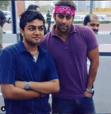 a man with a bandana on his head stands next to another man with his arms crossed