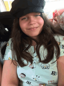 a girl wearing a hat and an owl shirt smiles for the camera