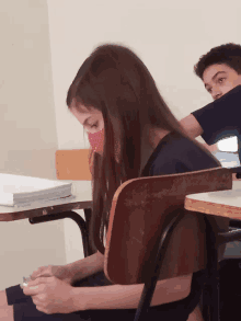 a girl wearing a red mask sits in a classroom