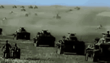 a row of military tanks are driving down a dirt road in a field .