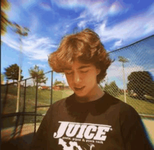 a young man wearing a juice t-shirt is standing in front of a fence .