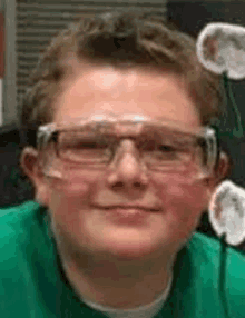 a young boy wearing safety glasses and a green shirt is smiling for the camera .