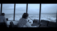 a woman is sitting at a desk in an airport control tower looking out the window .