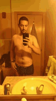 a shirtless man is taking a selfie in front of a mirror in a bathroom .