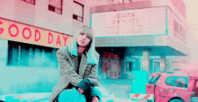 a woman is sitting on a car in front of a building with a sign that says `` good day '' .