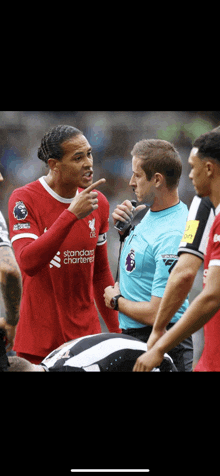 a soccer player wearing a red shirt that says standard chartered talks to a referee