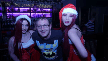 a man wearing a batman shirt poses for a picture with two women in santa hats