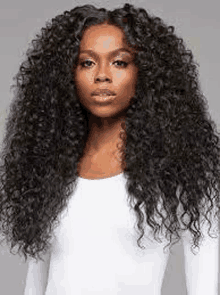 a woman with long curly hair is wearing a white shirt and looking at the camera .