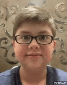 a young boy wearing glasses is making a funny face in front of a wall .