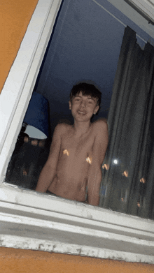 a shirtless boy looks out a window at night