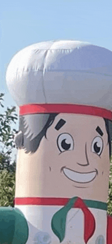 a giant inflatable chef is smiling and wearing a chef 's hat and apron .