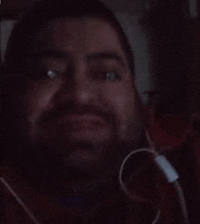 a man with a beard is wearing headphones and looking at the camera in the dark .