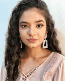 a close up of a woman 's face wearing earrings and a pink shirt