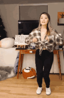 a woman wearing a plaid shirt and black pants is dancing in a living room