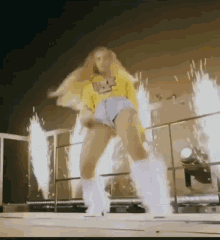 a woman in a yellow sweater and shorts is dancing on a stage