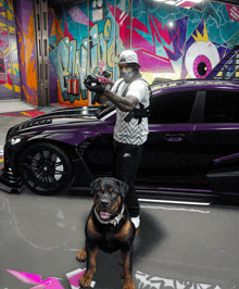 a man standing next to a dog in front of a purple car with graffiti on it